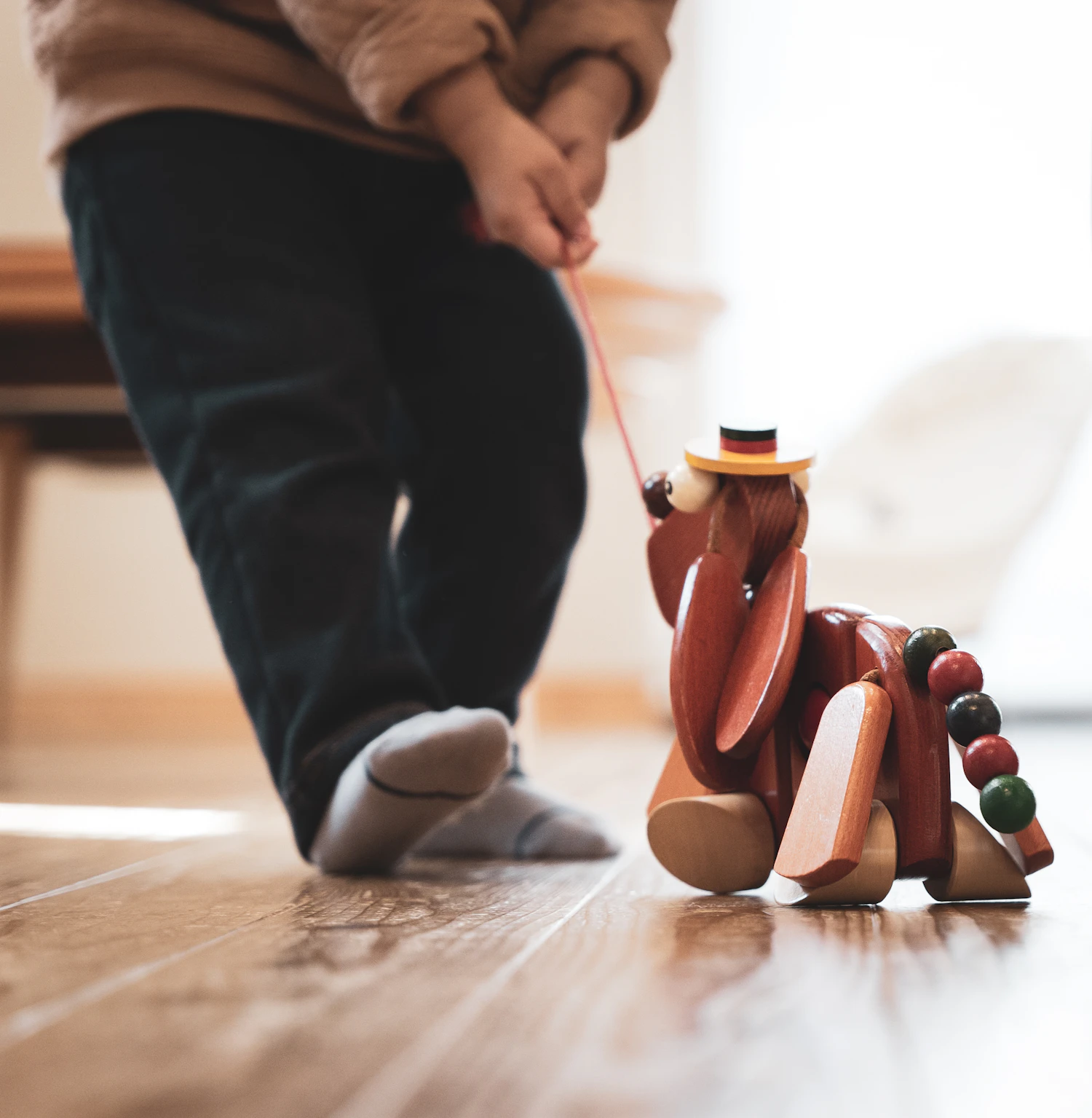 A child pulling a wooden hound toy along a wooden floor by a red cord — Pull-Along Hound, in stock