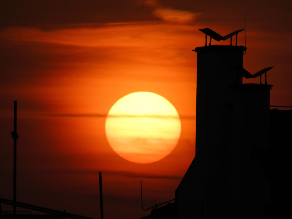 the sun is setting behind a building with a bird on top