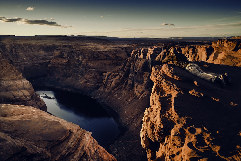 a man laying on top of a cliff next to a lake