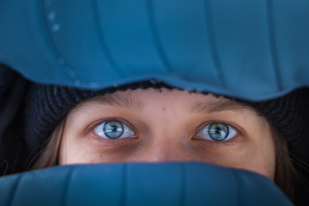 a girl with blue eyes peeking out from behind a chair