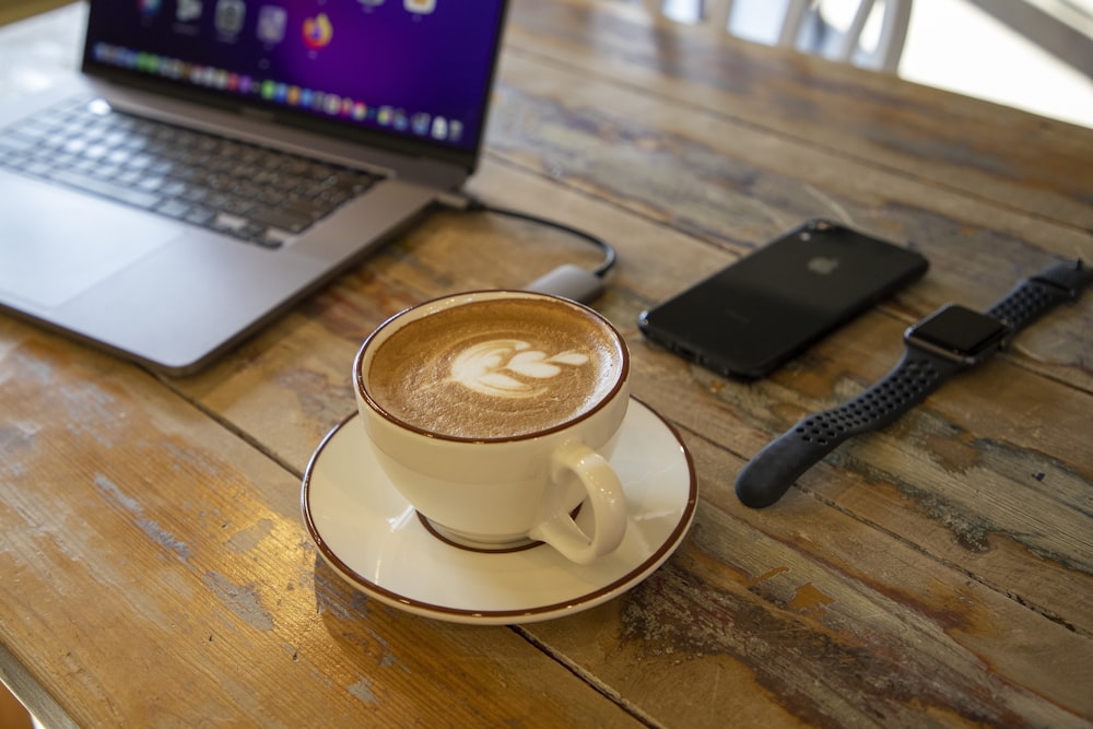 a cup of coffee on a saucer in front of a laptop