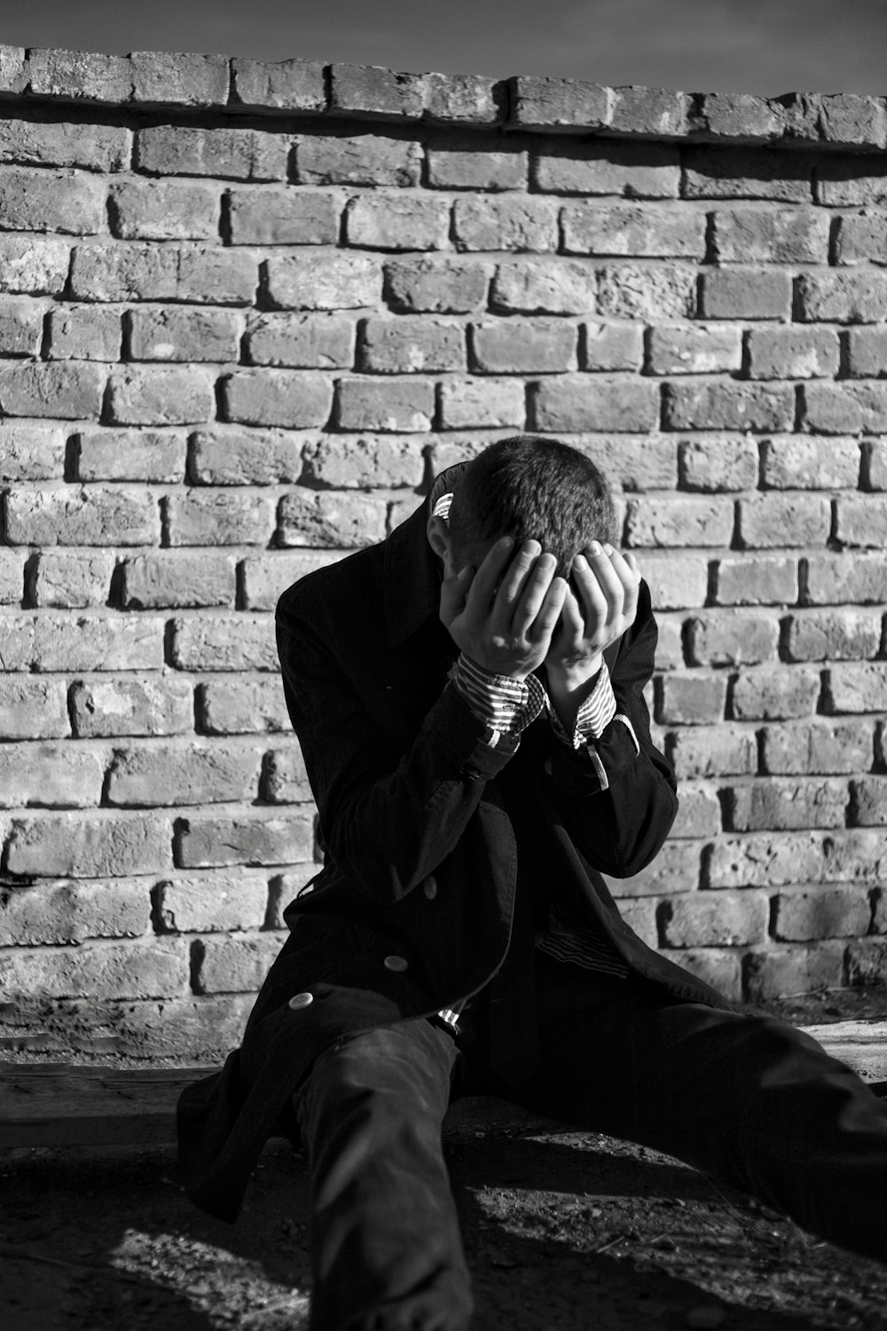 a man sitting on the ground covering his face with his hands