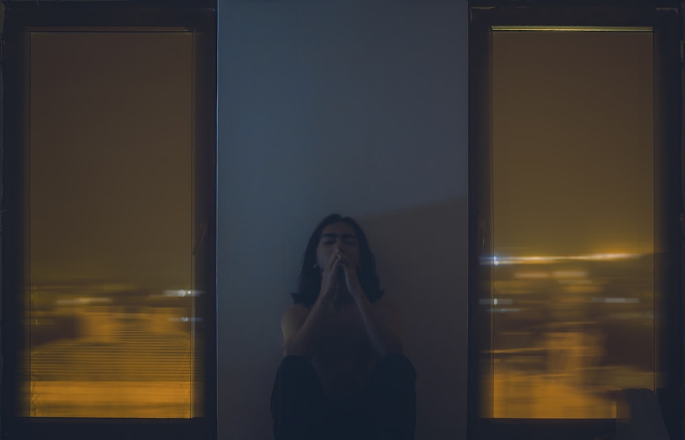 a woman covering her face in front of a window