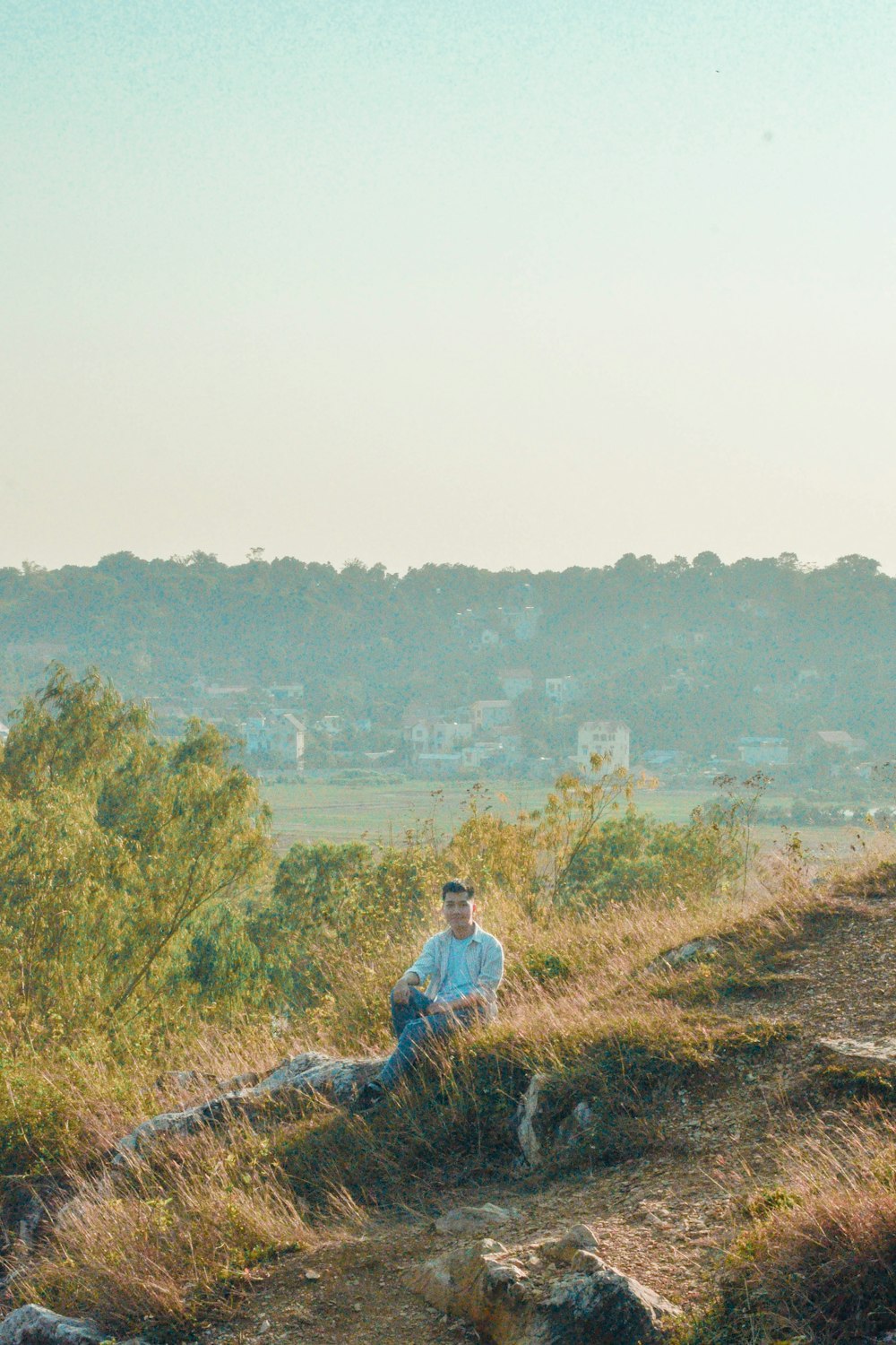 a man sitting on top of a hill next to a cow