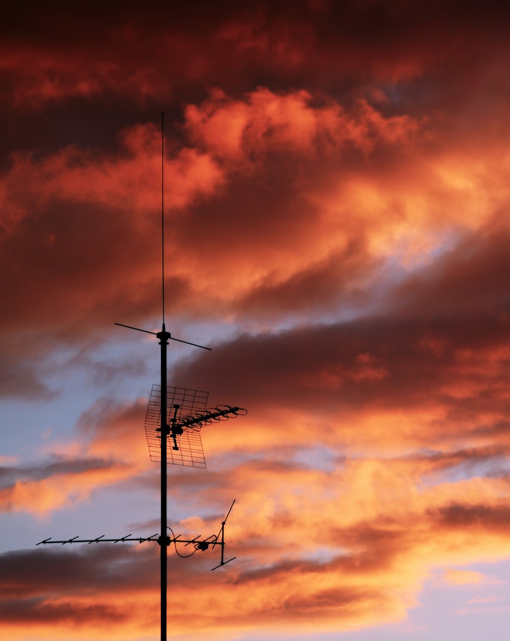 Un cielo rojo con nubes y una antena de televisión