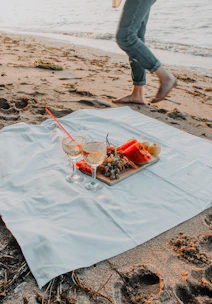 A waterproof picnic mat laid out on a sandy beach with waves gently rolling in the background.