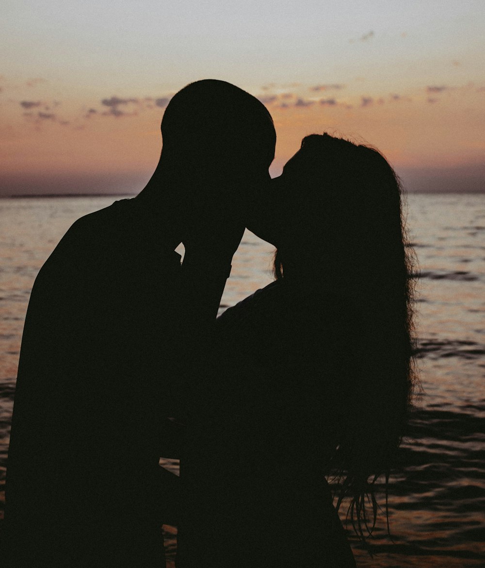 um homem e uma mulher se beijando na frente de um corpo de água