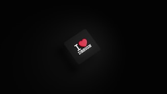 A dark background with a black square in the center. The square has the text 'I ❤️ DESIGN' with the heart symbol in red color.