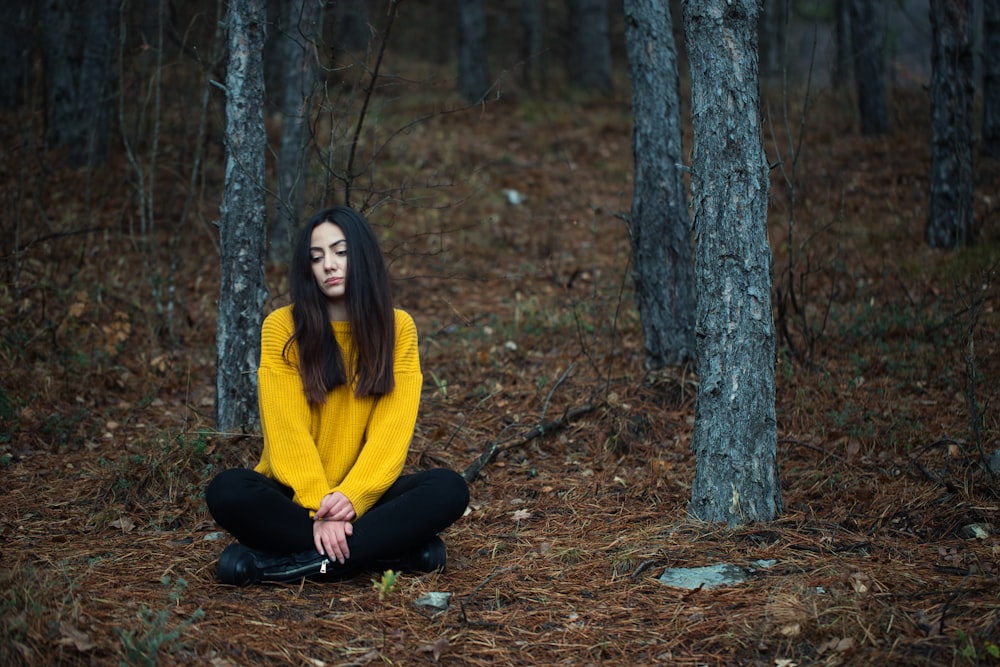 a woman in a yellow sweater is sitting in the woods