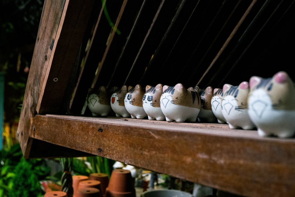 uma fileira de gatos de cerâmica sentados em cima de uma prateleira de madeira
