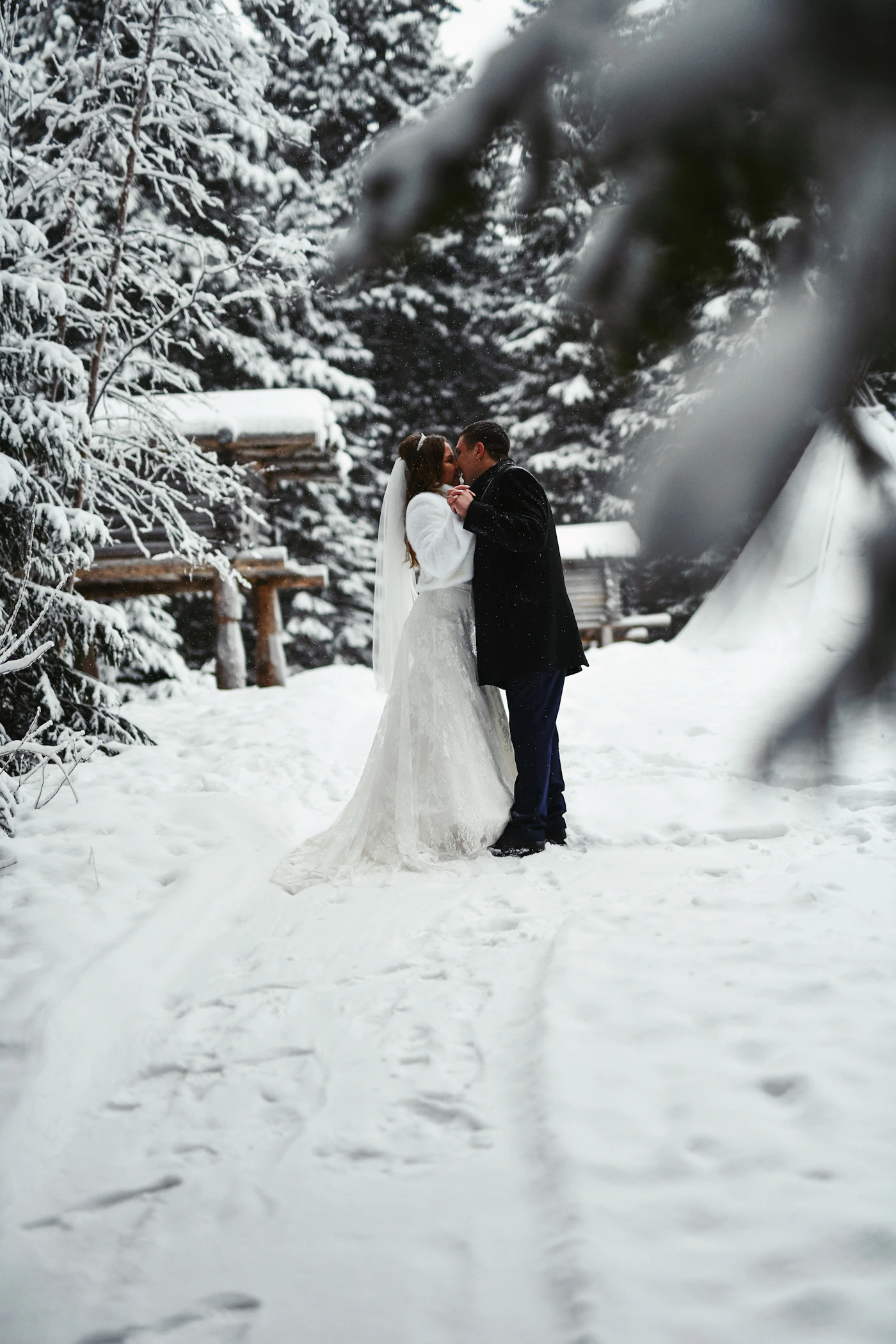 Bride and groom sharing their first kiss in a romantic moment surrounded by falling snow in a winter wedding