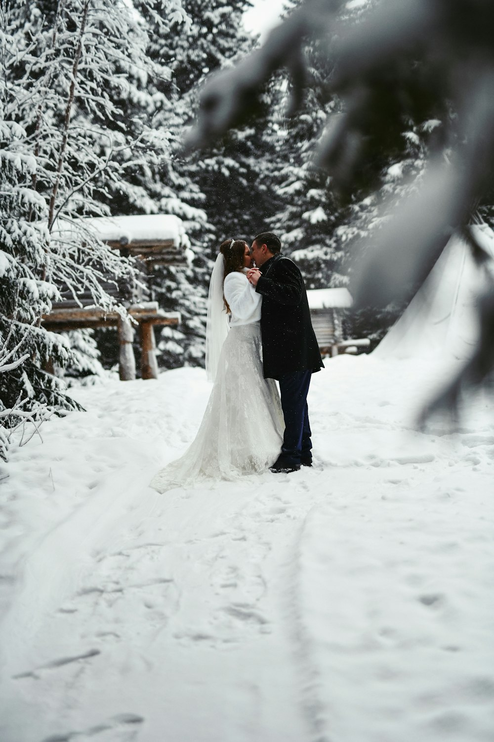 a bride and groom kissing in the snow