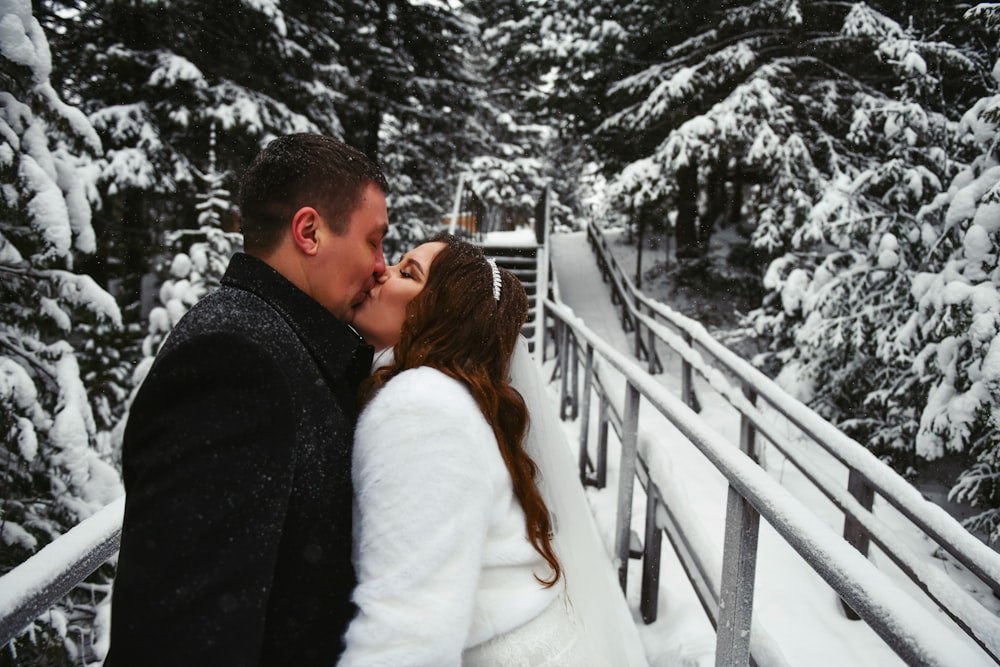 a bride and groom kissing on a bridge in the snow
