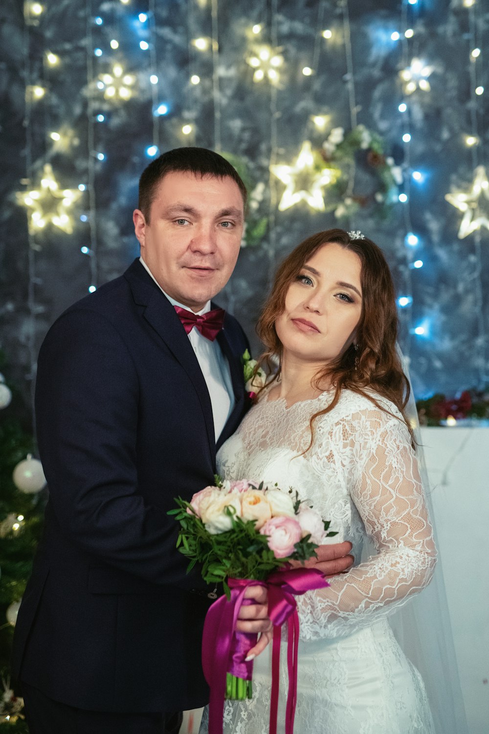 a bride and groom posing for a picture in front of a christmas tree