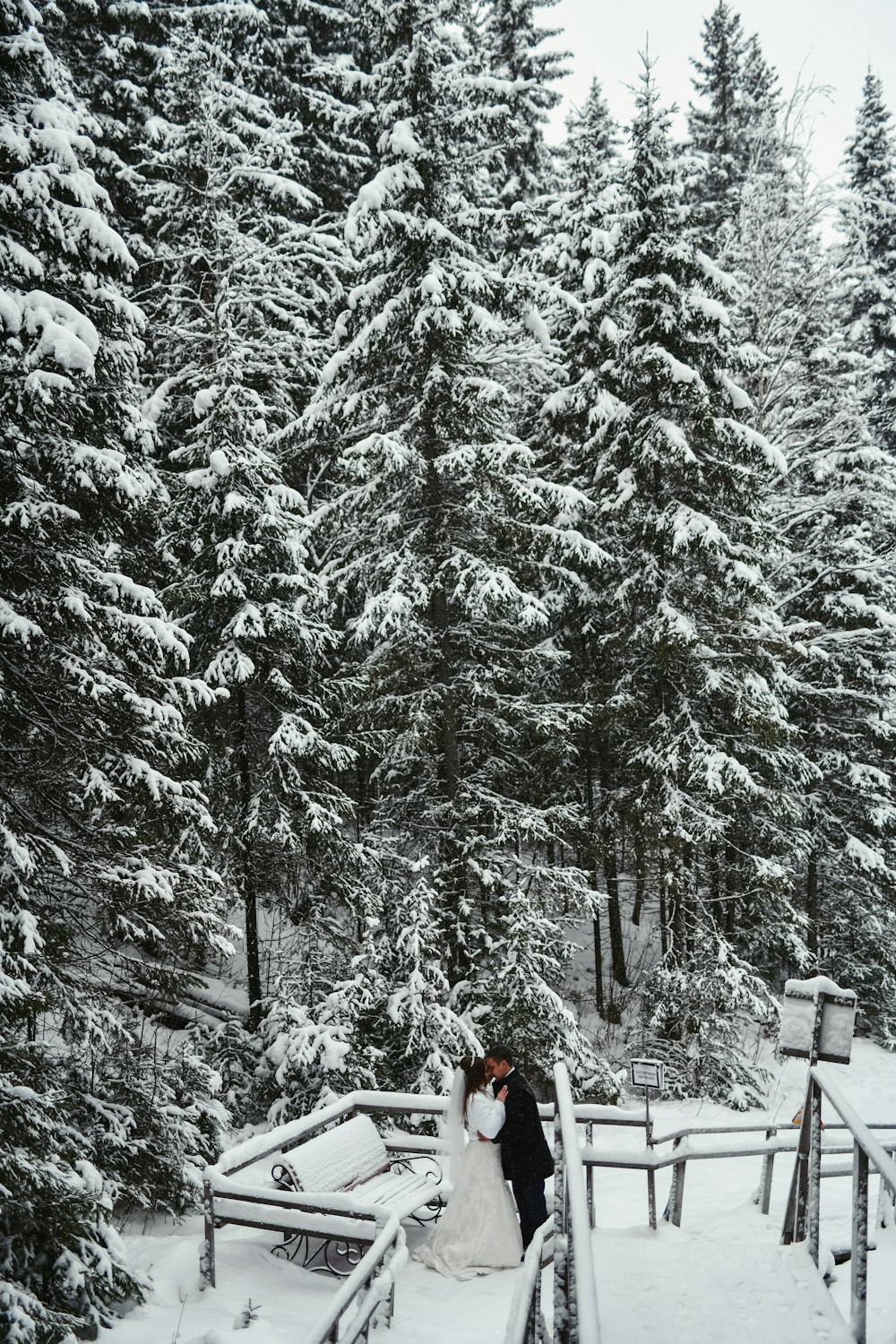 a bride and groom standing on a bridge in the snow