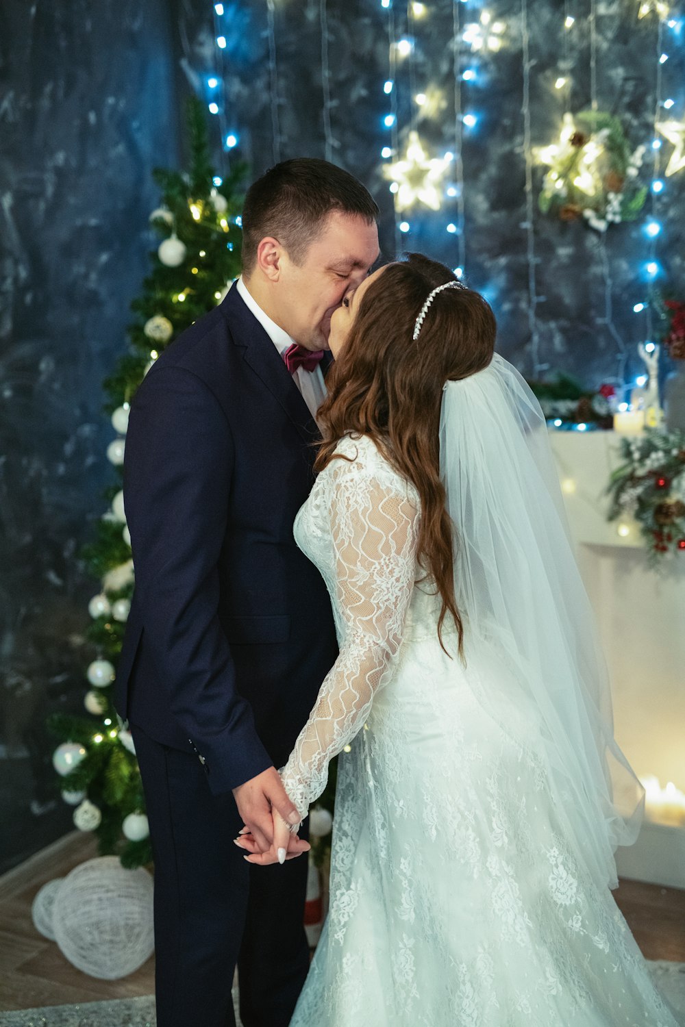 a bride and groom kissing in front of a christmas tree