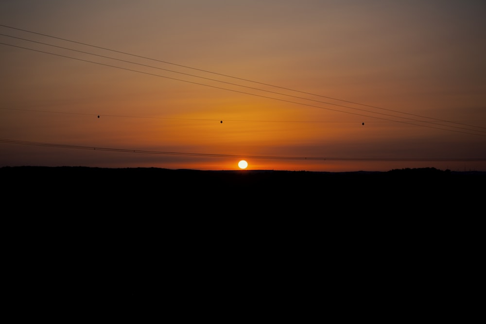 the sun is setting over a field with power lines