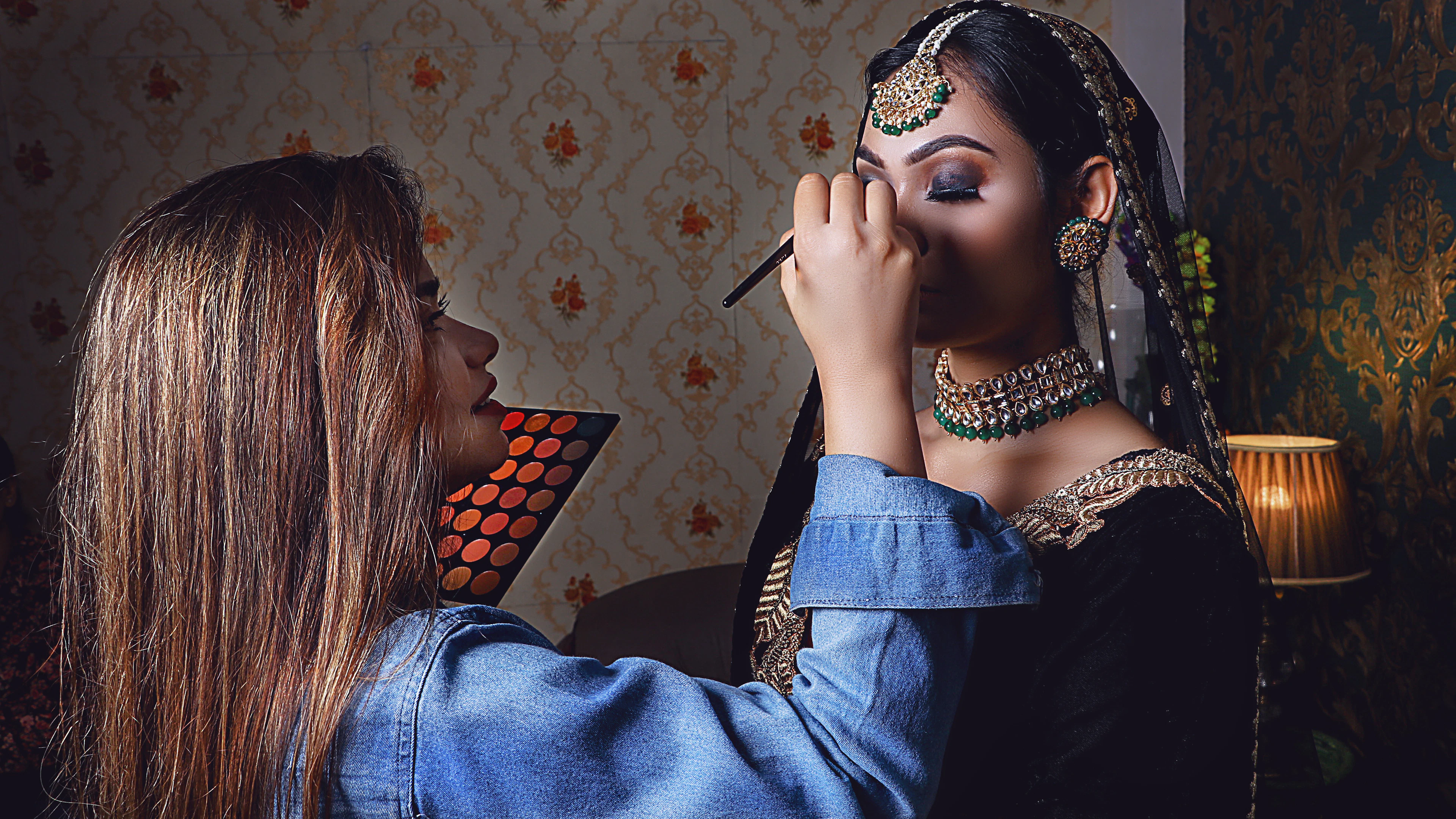 A makeup artist holding a palette and shading the eyes of a bride in gold and green jewellery