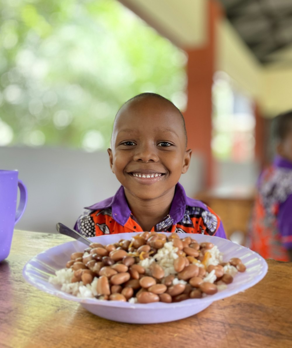 a young boy sitting at a table with a plate of food