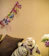A small cat wearing a colorful handmade dress sitting on a cozy cushion.