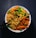 A bowl filled with instant noodles topped with a colorful array of vegetables, including sliced carrots, green bell peppers, peas, and corn. The dish is neatly arranged, with chopsticks resting on the side, creating a visually appealing and appetizing meal.