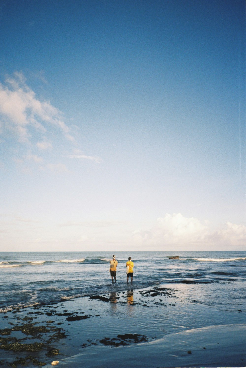 two people standing on a beach next to the ocean