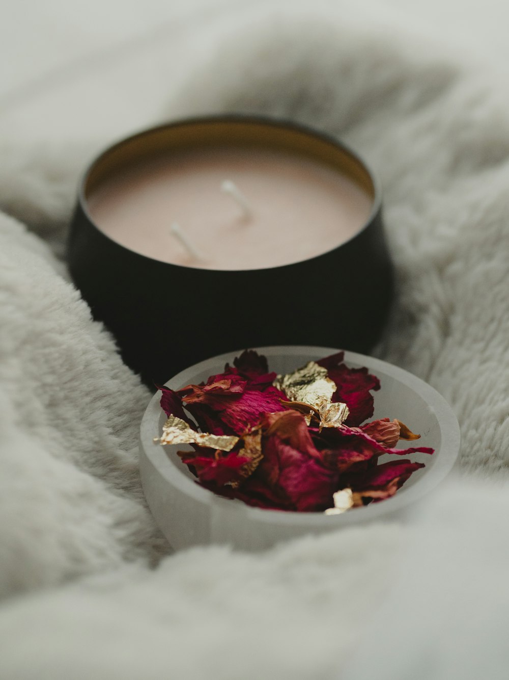 a bowl of rose petals next to a candle