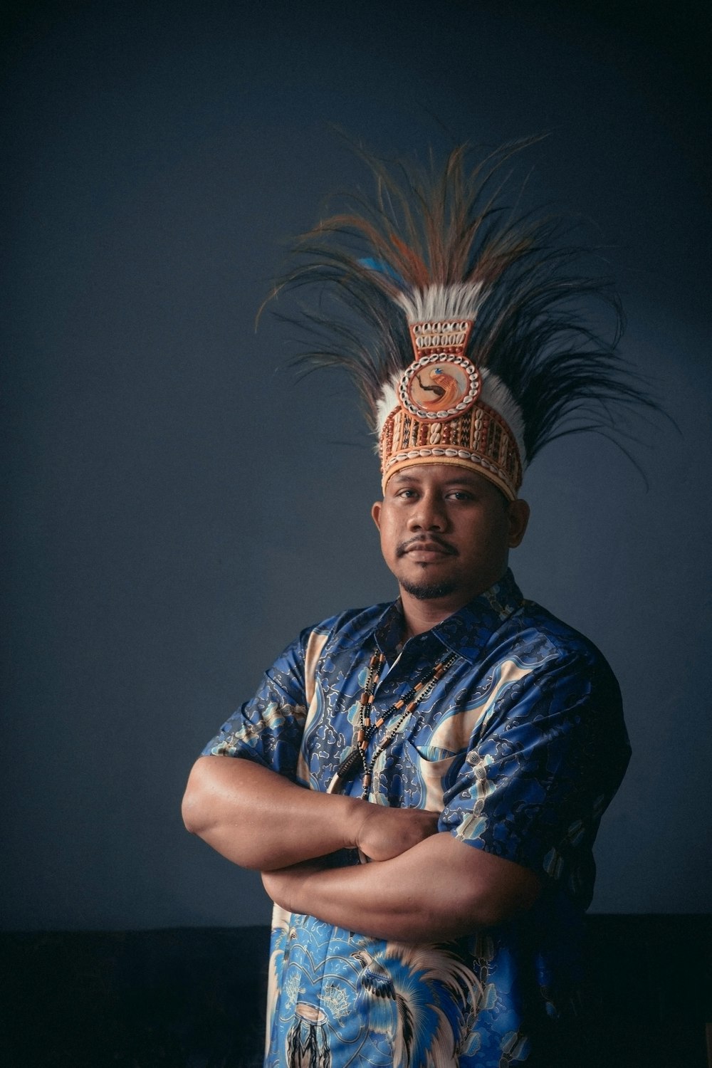 a man wearing a headdress standing with his arms crossed