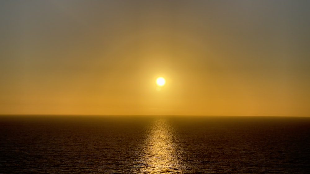 the sun is setting over the ocean on a cloudy day