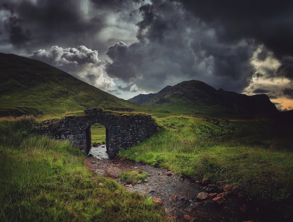 a stone bridge in the middle of a grassy field