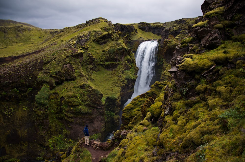 a man standing at the base of a waterfall