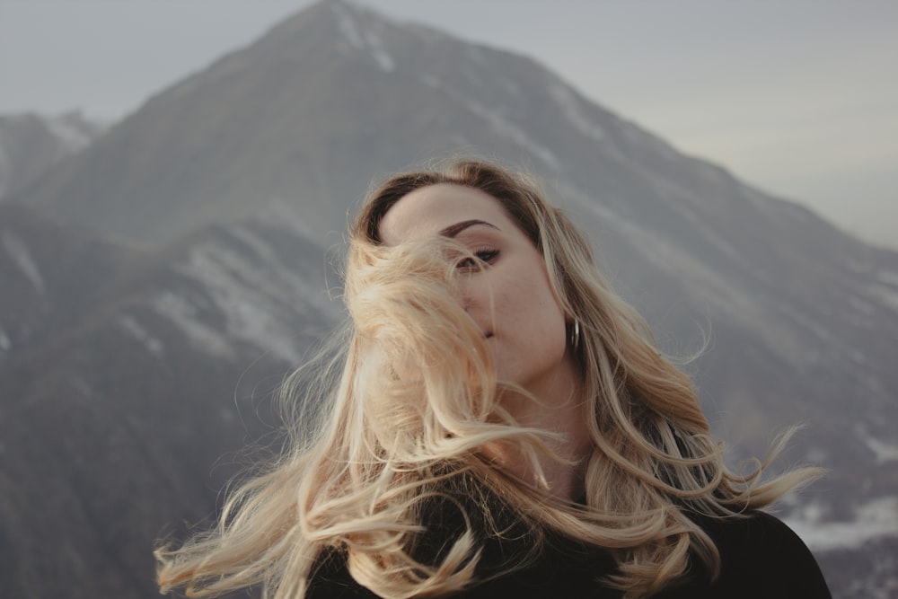 a woman with long blonde hair standing in front of a mountain