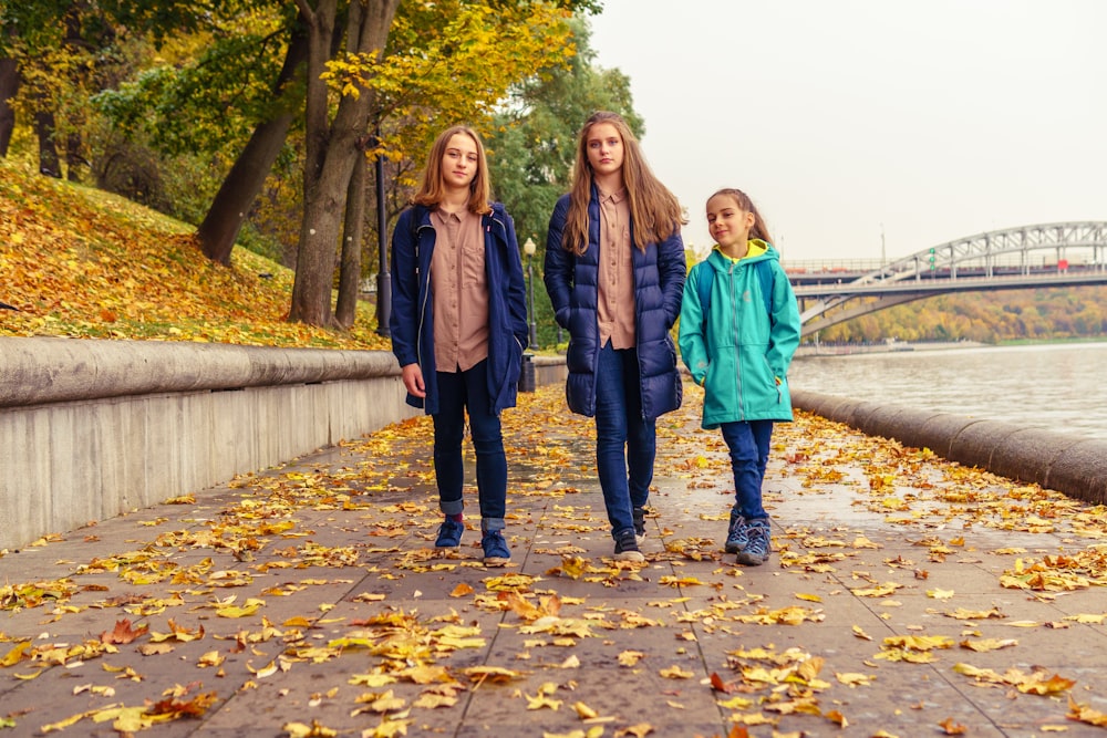 a group of three women walking down a sidewalk next to a river