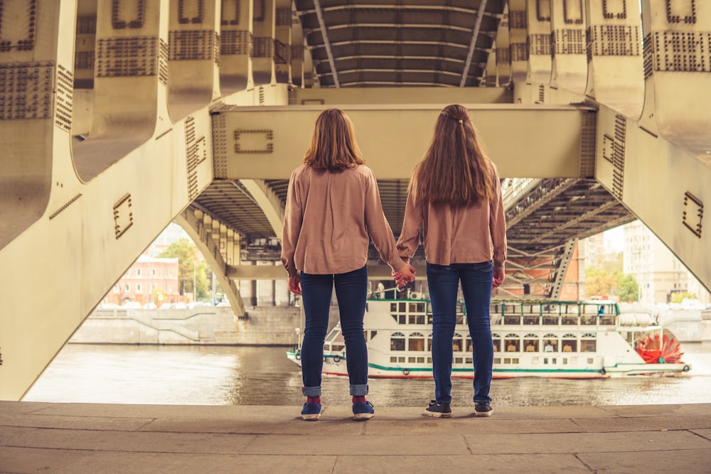 two women holding hands while standing under a bridge