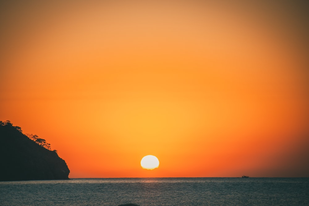 the sun is setting over the ocean with a mountain in the background