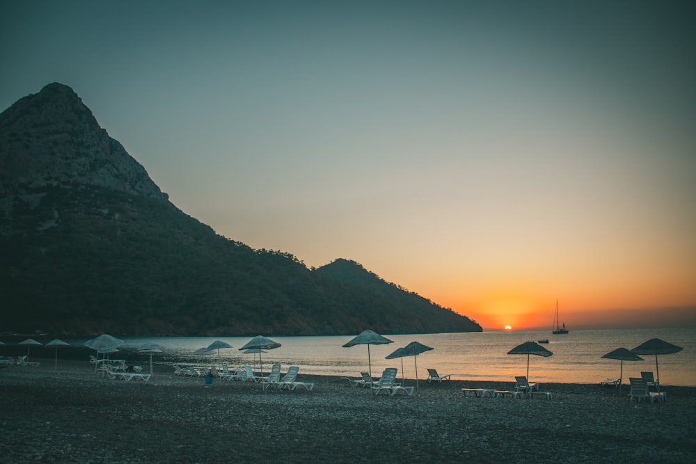 a beach with umbrellas and chairs and a mountain in the background