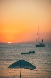 Golden sunset over a calm sea with a small sailboat drifting nearby.
