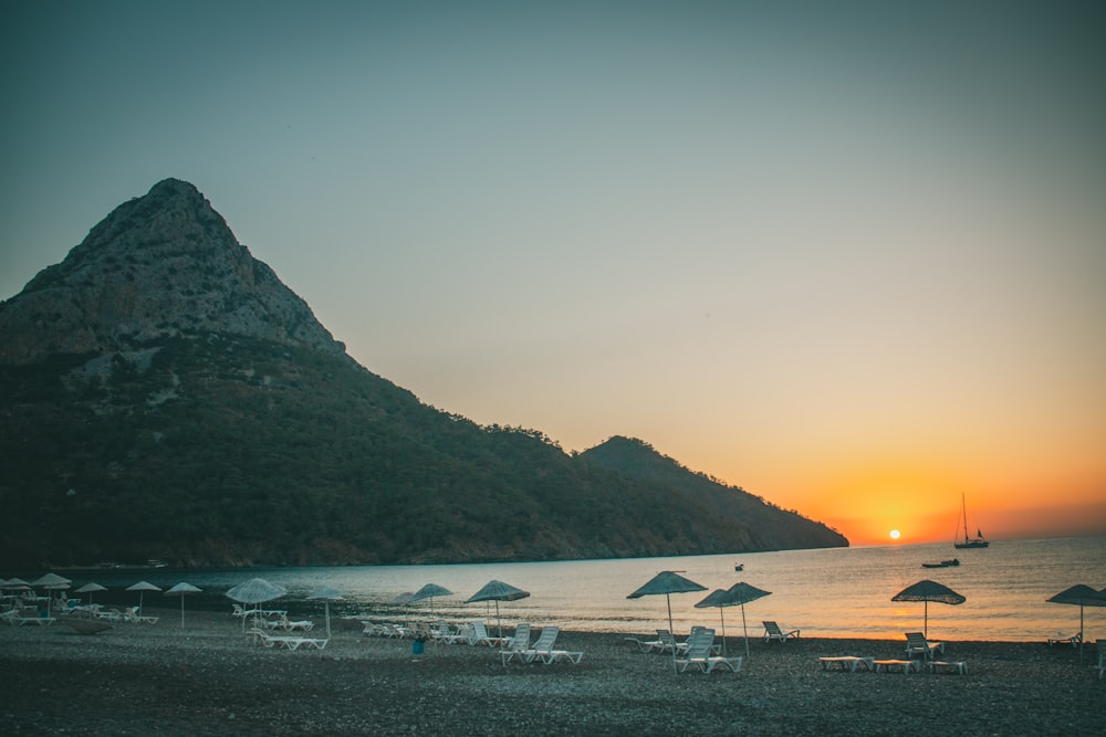 a beach with umbrellas and chairs and a mountain in the background