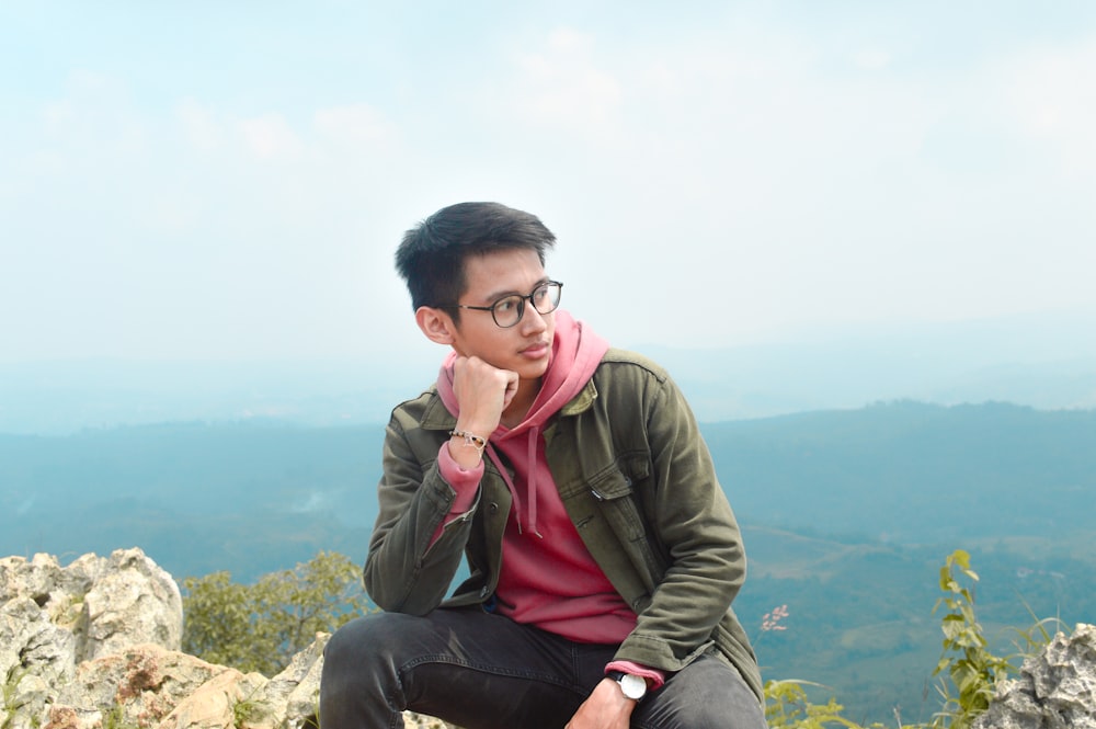 a man sitting on a rock with a pink scarf around his neck