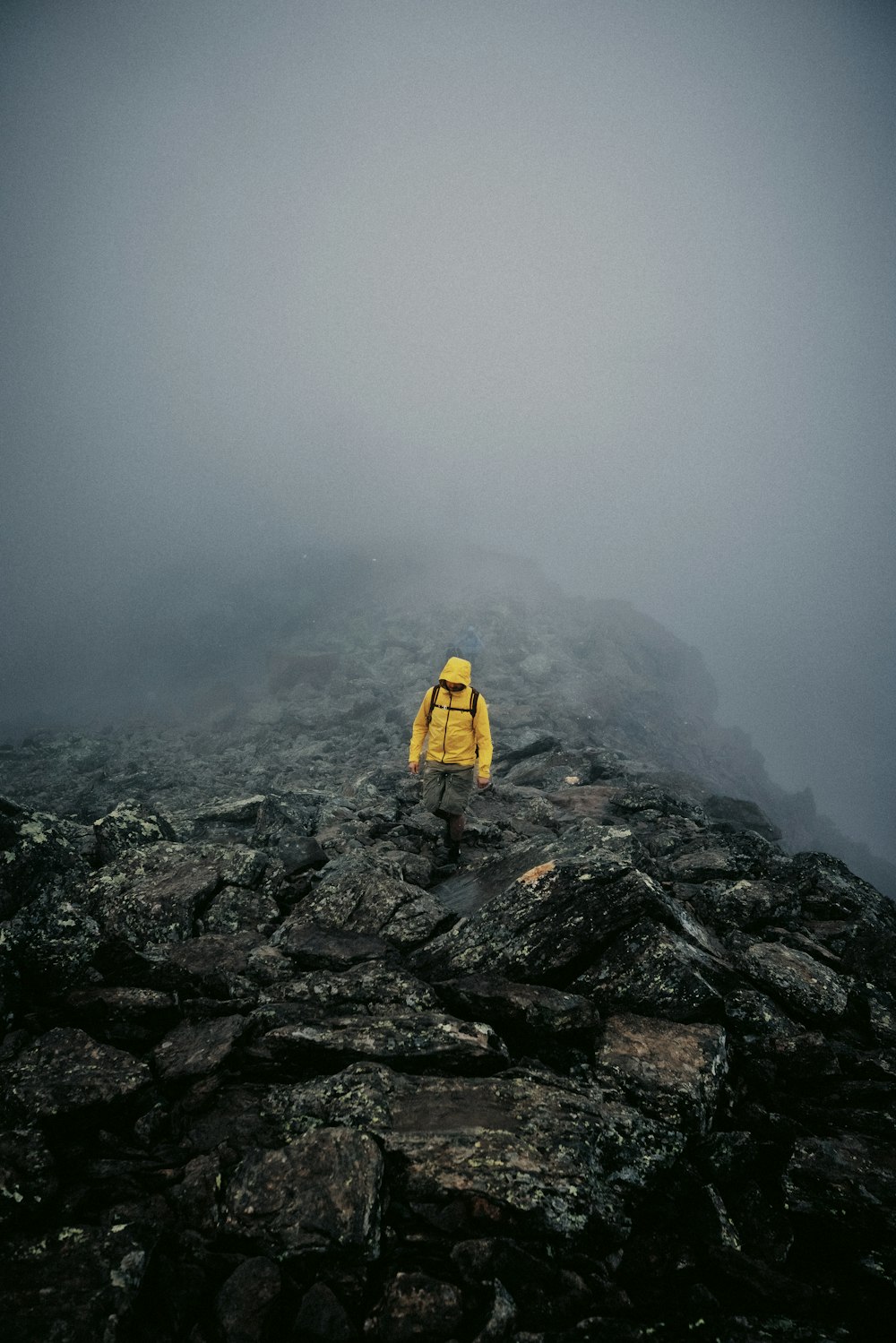 a person in a yellow jacket standing on a rocky mountain