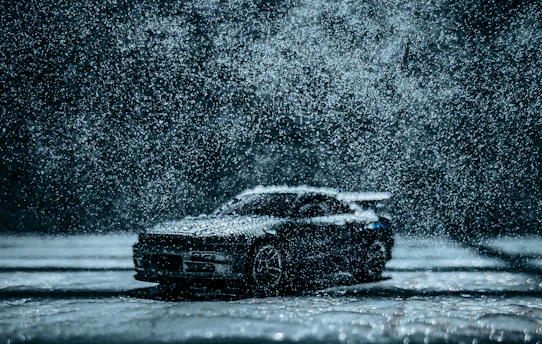 Dynamic shot of a car driving through rain, water visibly repelling off the coated surface.