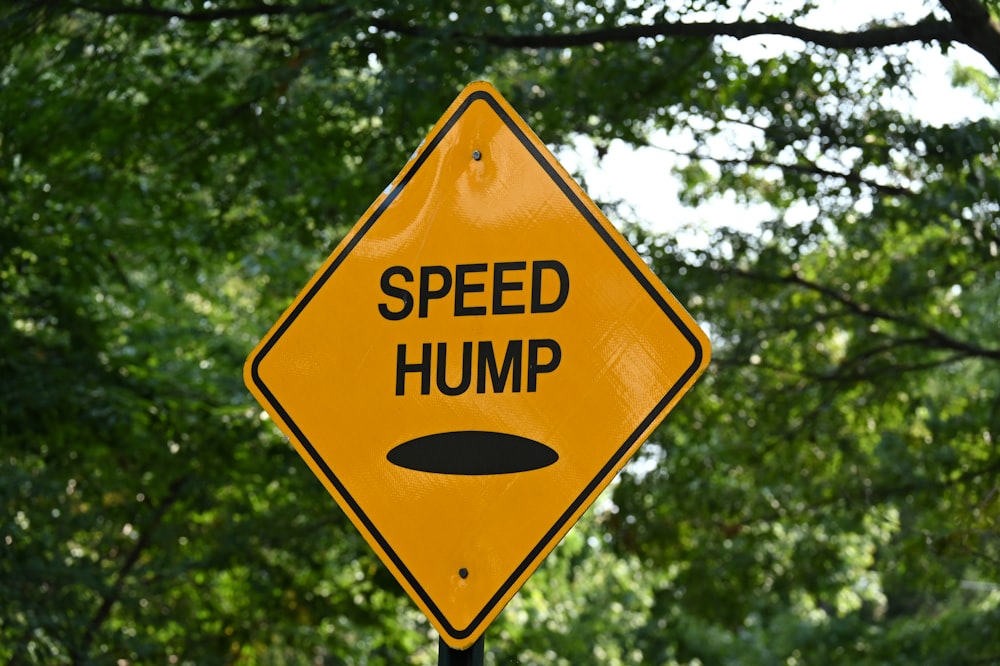 a yellow speed hump sign sitting next to a forest