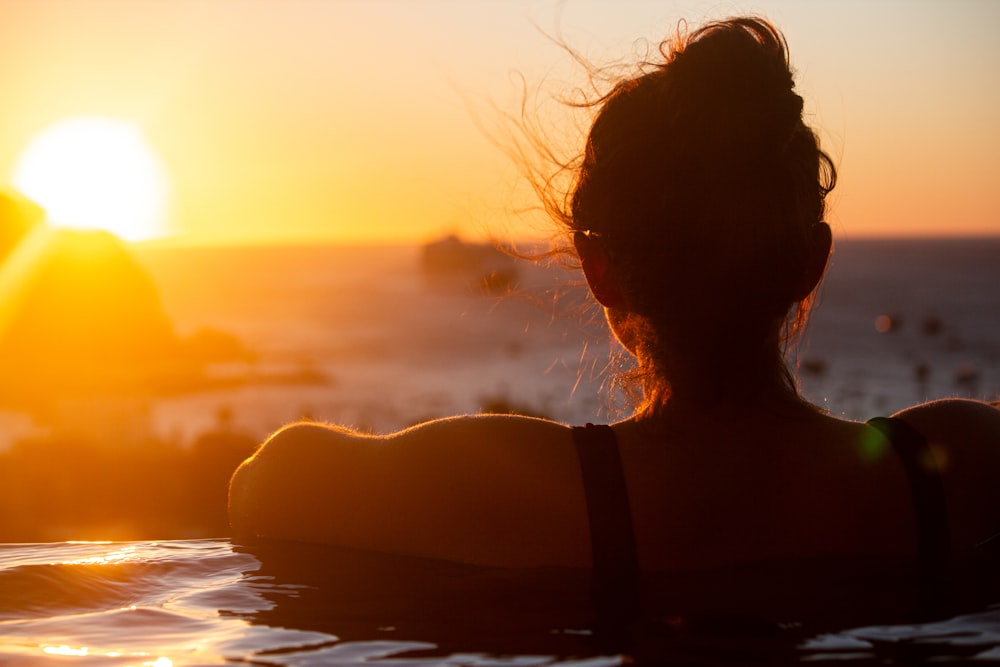 a woman is sitting in the water at sunset