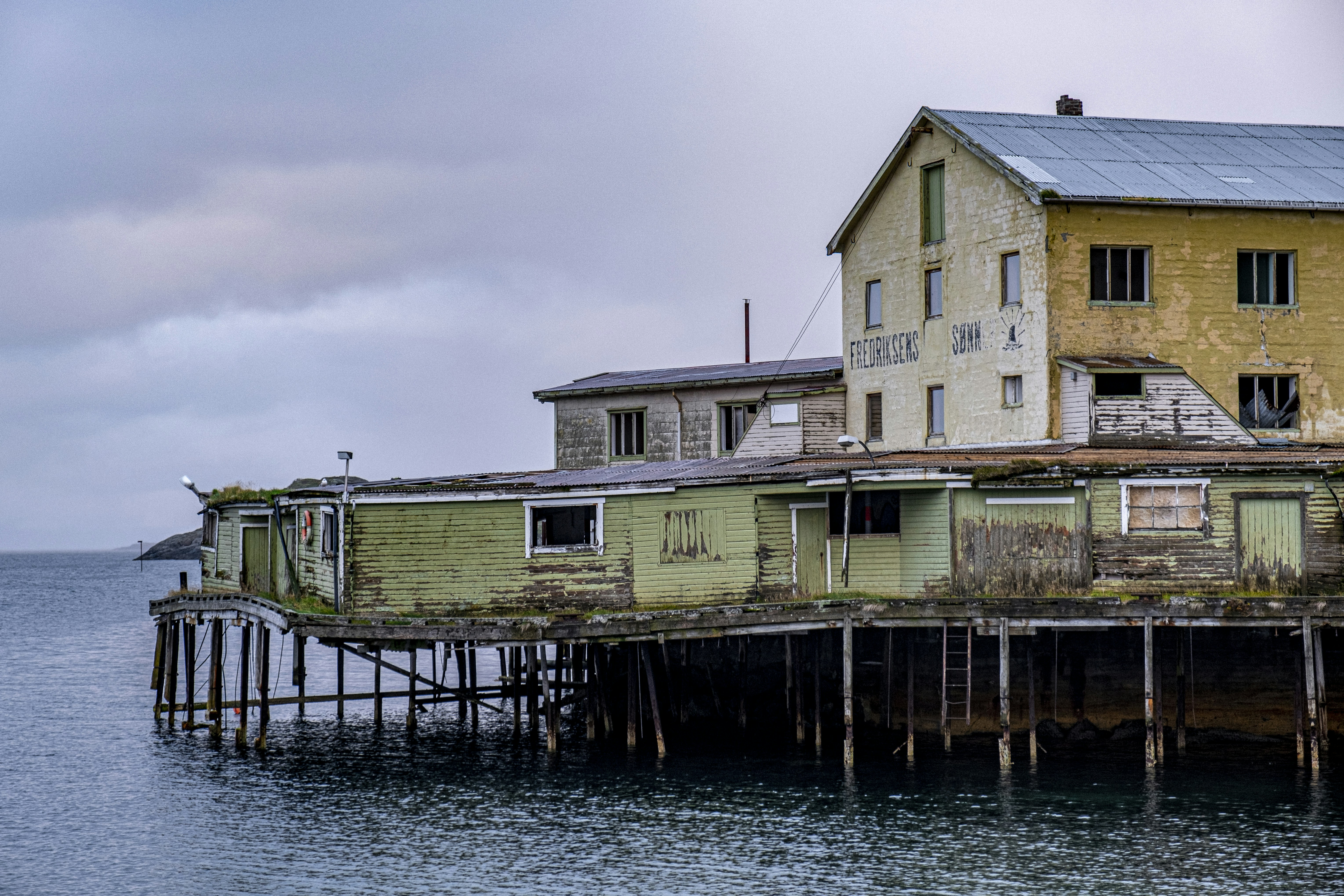 a yellow house sitting on top of a wooden pier, a fascinating abandoned fish factory, almost collapsing
