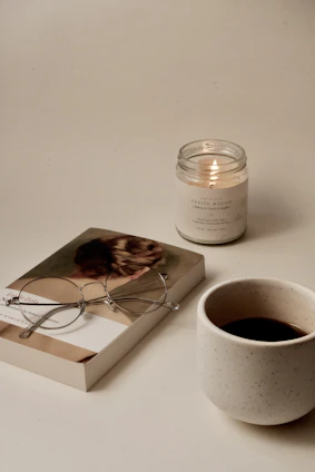 A cozy scene with a glowing lumaura candle beside a book and a cup of tea on a wooden table.
