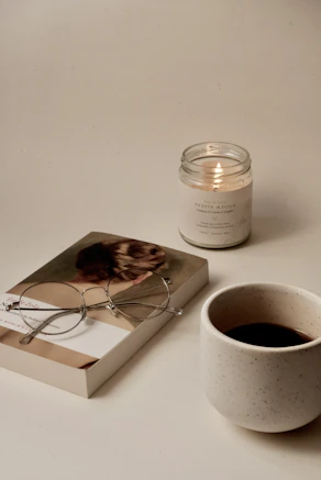 a cup of coffee next to a candle and a book with glasses on top representing clarity and confidence