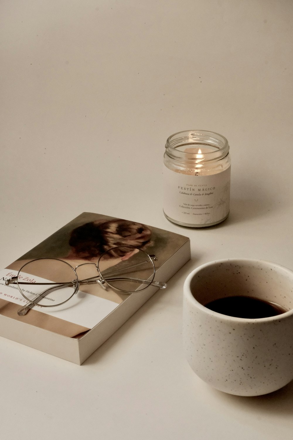 a cup of coffee next to a book and candle