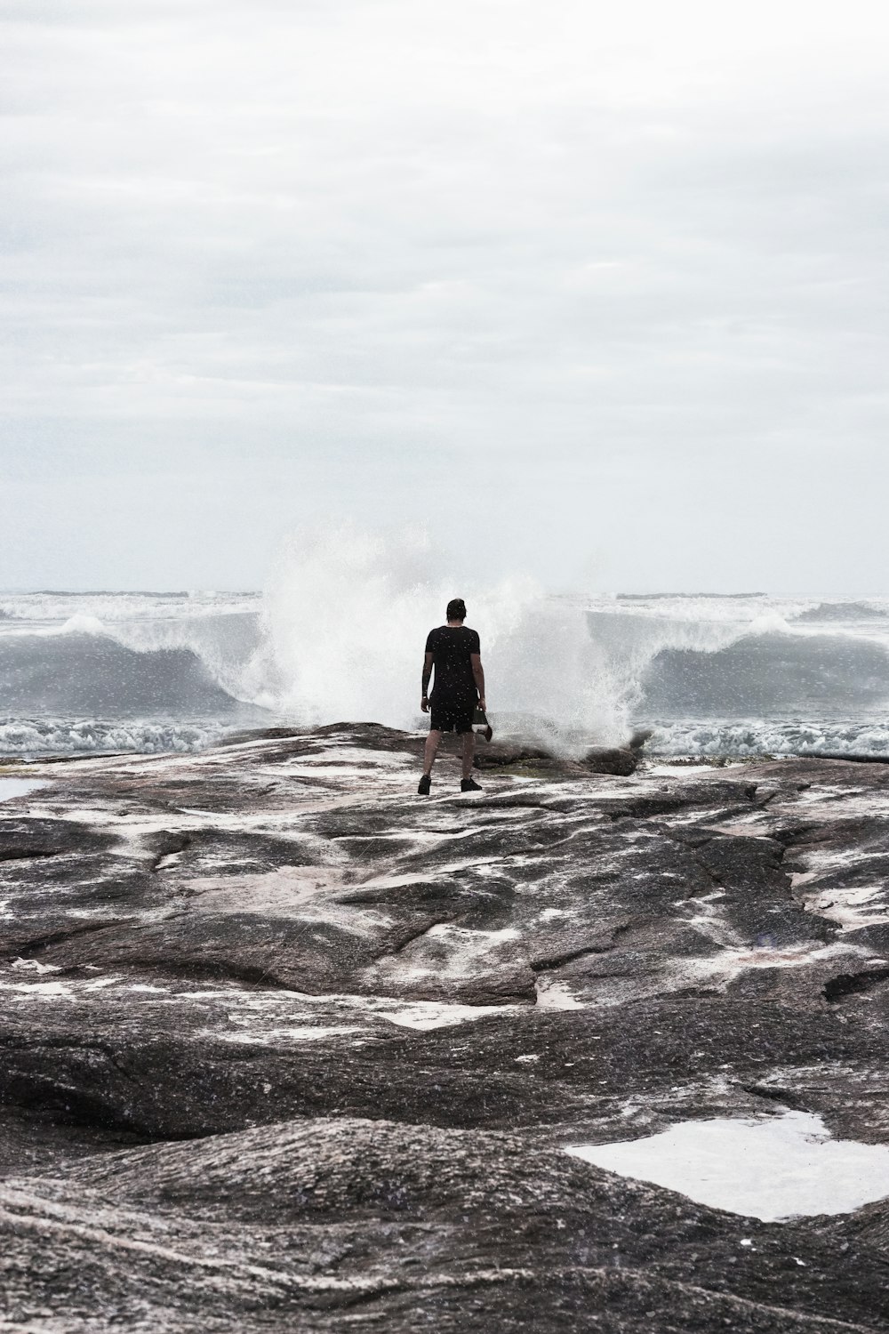 a man standing on top of a rocky beach next to the ocean