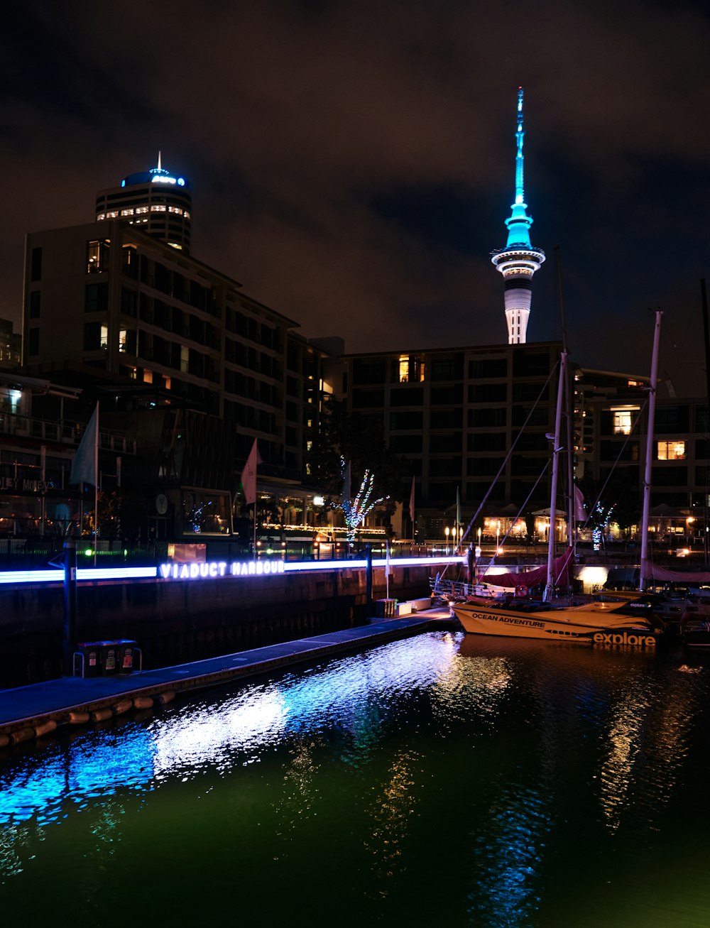 a night scene of a harbor with boats and a tower in the background