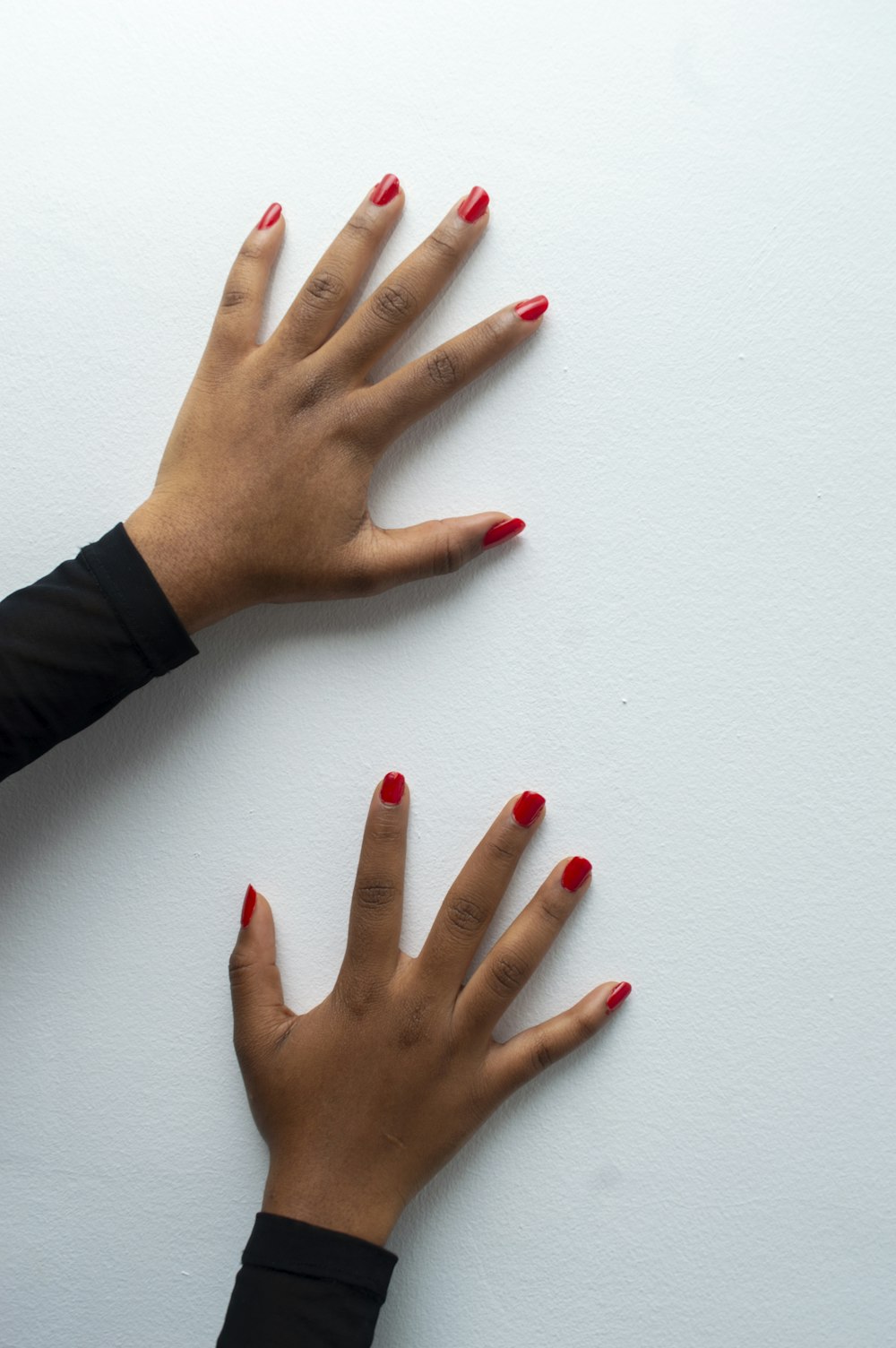 a pair of hands with red nail polish against a white wall